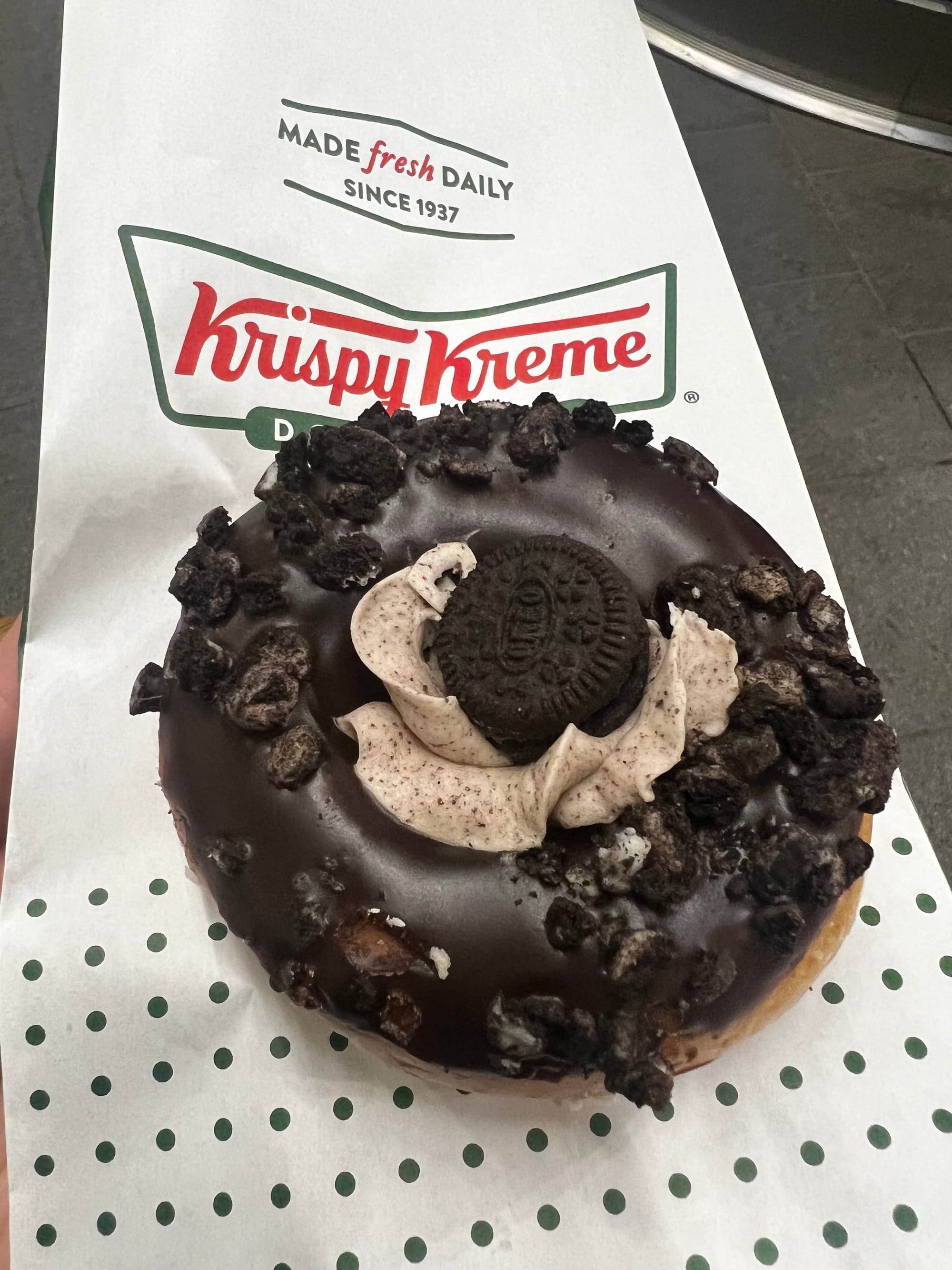 A stacked Krispy Kreme cookie donut sitting on a Krispy Kreme wrapper.