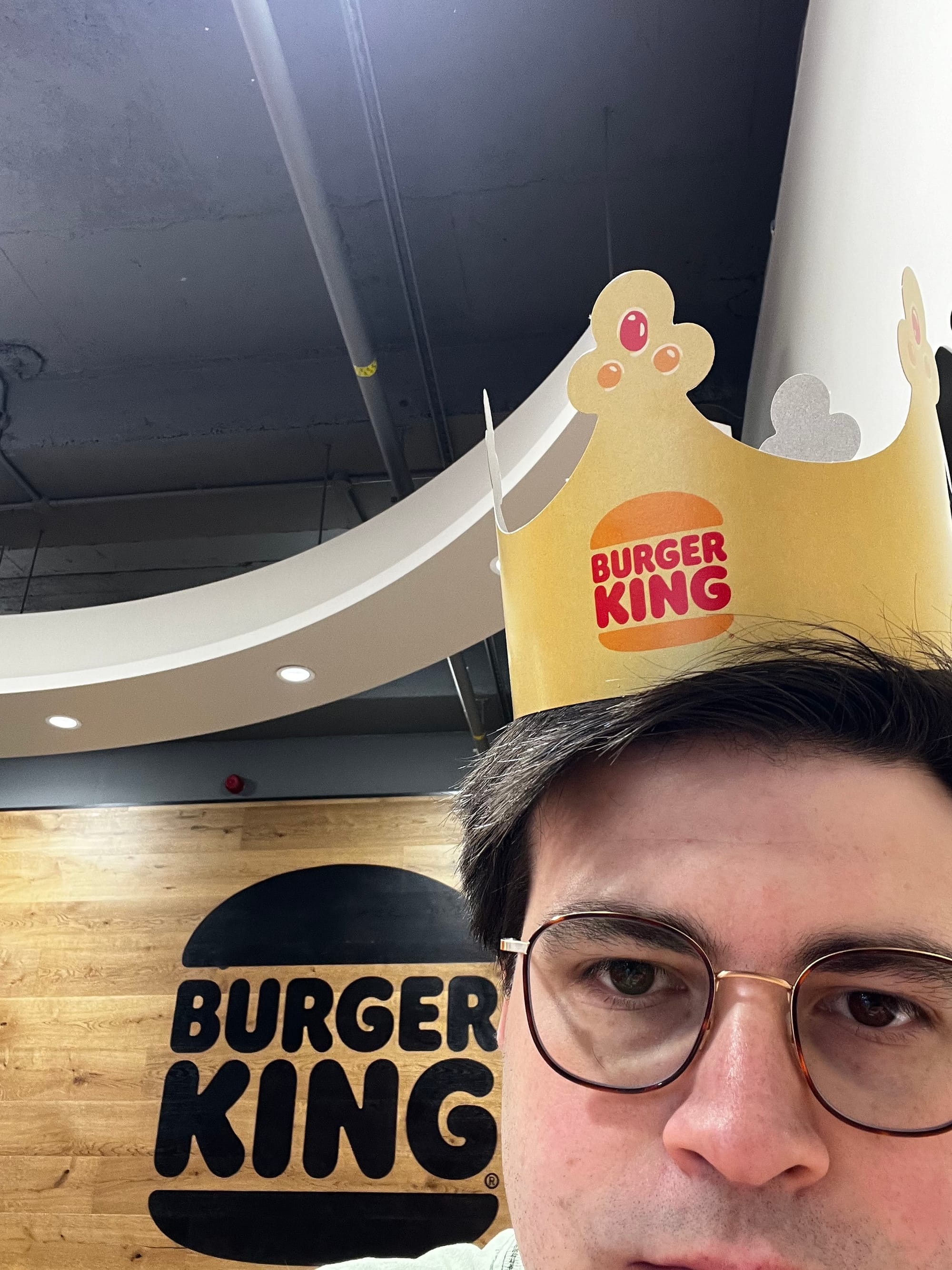 The author sits in front of the Burger King logo while wearing a Burger King crown.