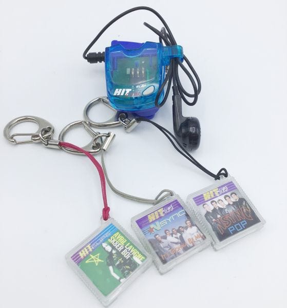 A small, plastic HitClips player, with a single earbud wired to it, with three cartridges for *NSYNC and Avril Lavigne songs.
