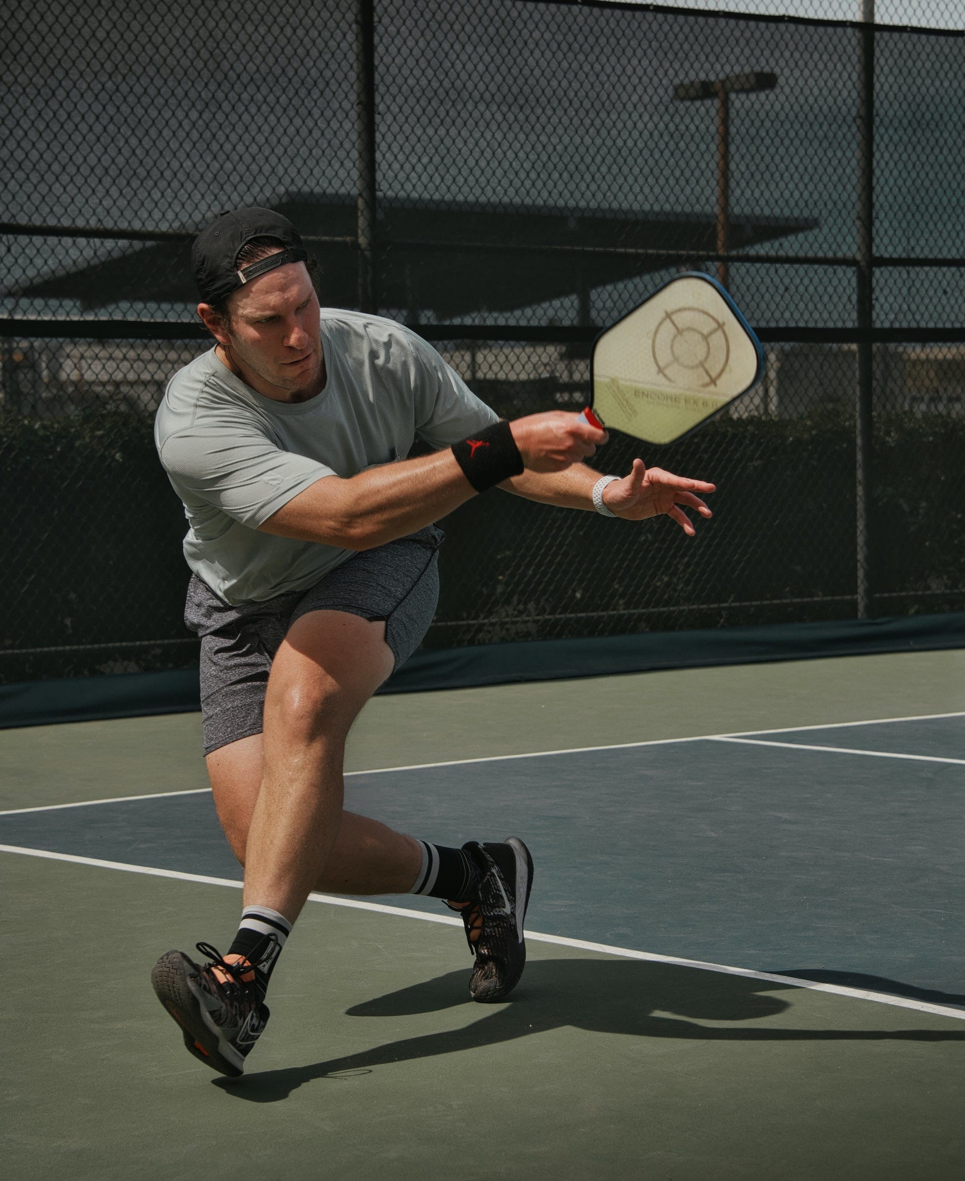 An athletic male steps forward while swinging a pickleball paddle.