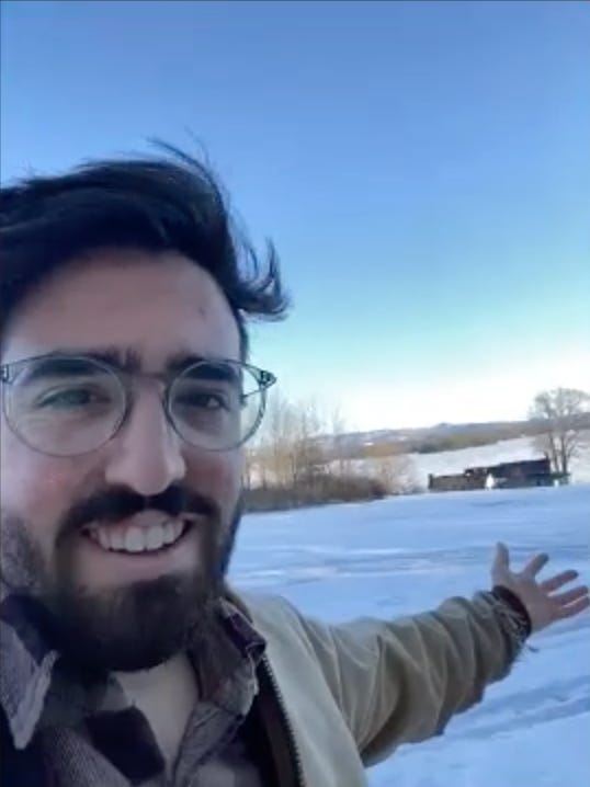 Bearded man with arm outstretched, showing off snowy tundra.