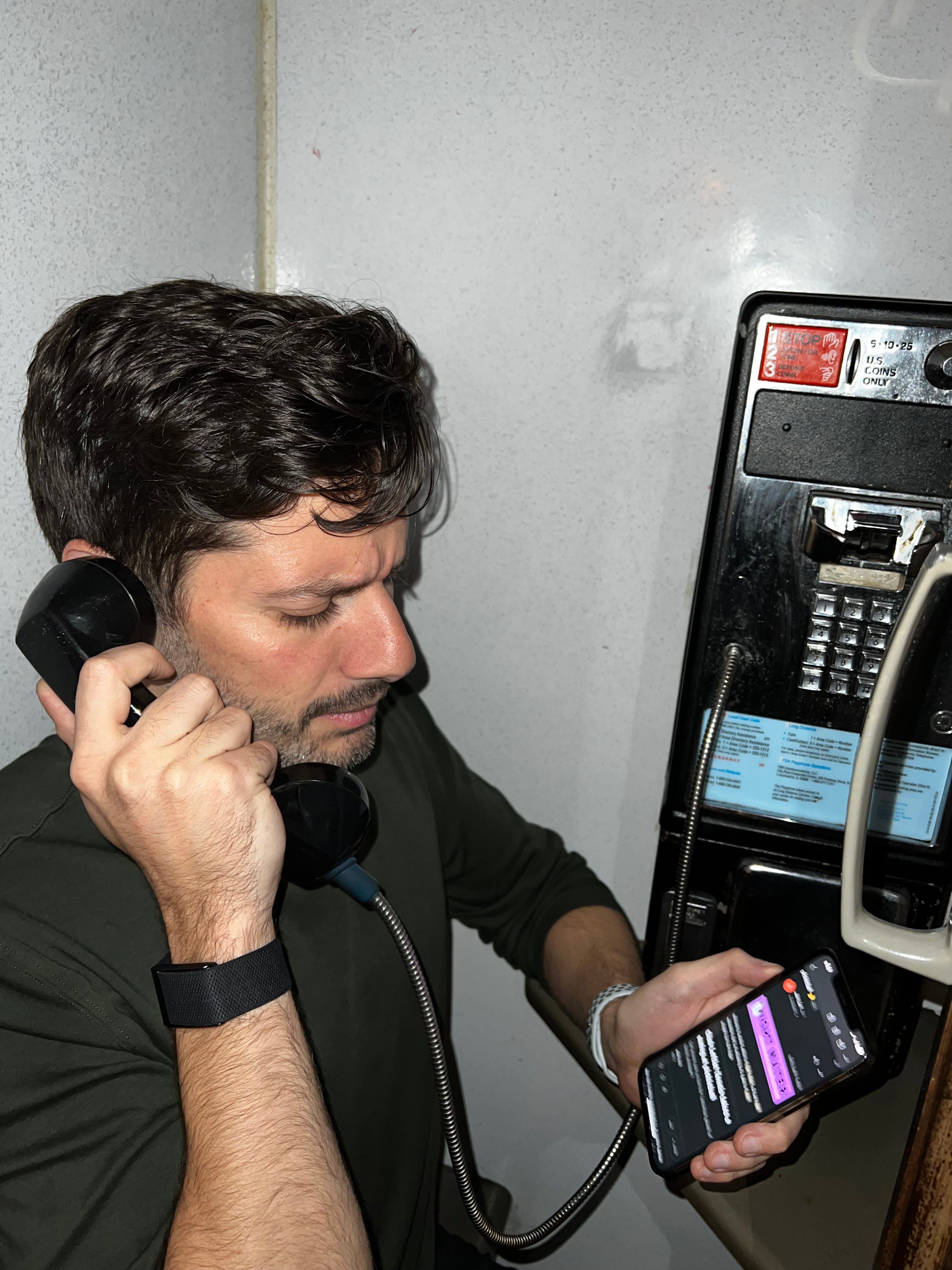 Sami talks on a public phone while holding a phone open to Night Water.