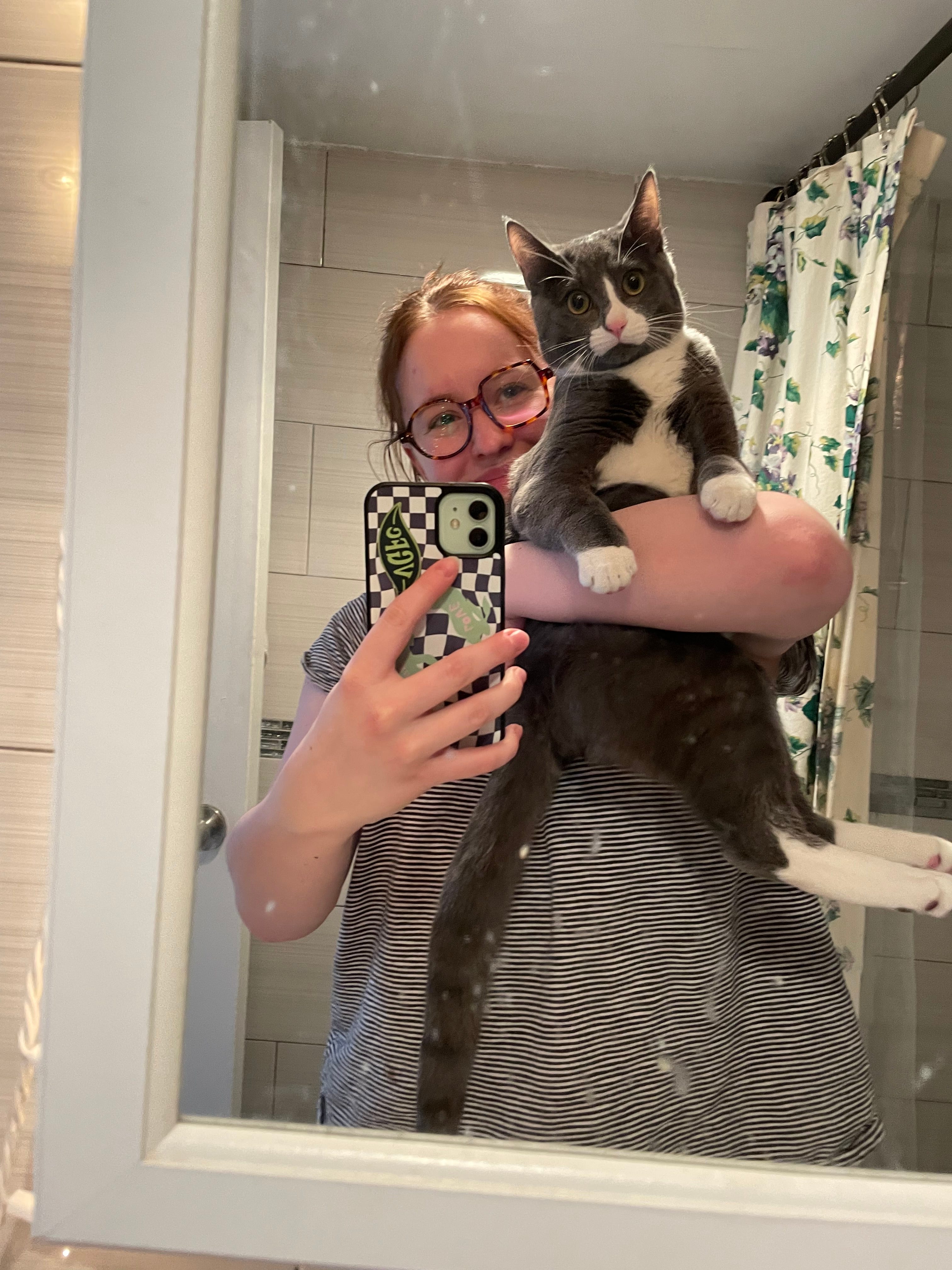 Woman taking a mirror selfie with her grey and white cat.