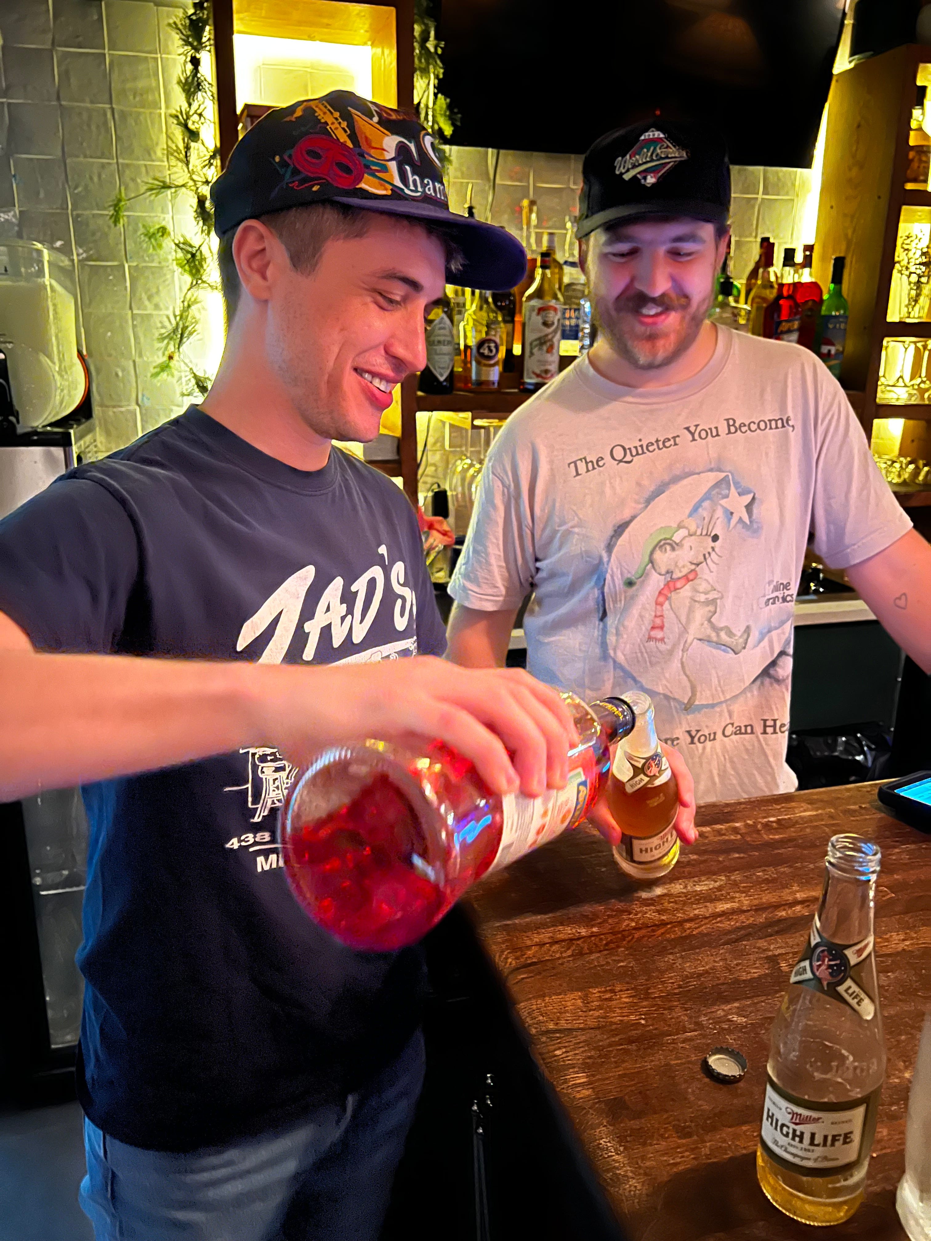 Two men in baseball caps behind the bar making a beer cocktail with Aperol.