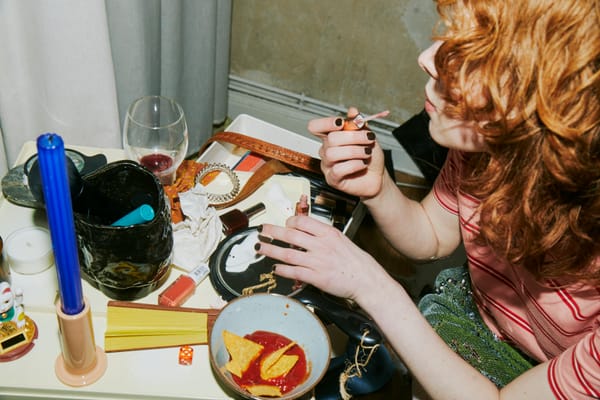 A woman applies lip gloss over a messy table.
