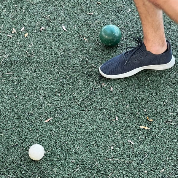 Two bocce balls on turf near feet.