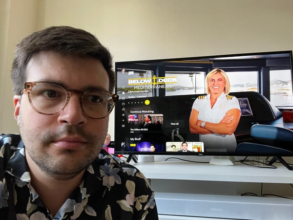 A man in glasses crouches in front of a TV open to the Peacock app.