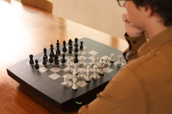 A man sits in front of a Square Off robotic chessboard.