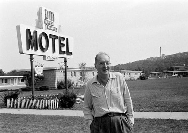 Vladimir Nabokov standing in front of a motel sign.