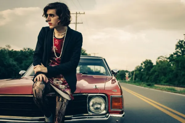 Singer Ezra Furman sits on the hood of a classic car.