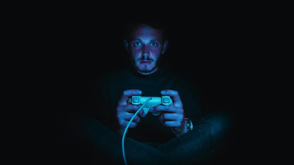 A man sits in darkness with a game controller in his hands.