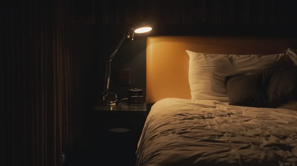 A lit up lamp next to an empty bed.
