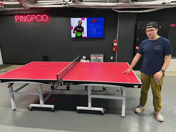 Man stands, touching ping pong table at PingPod location.