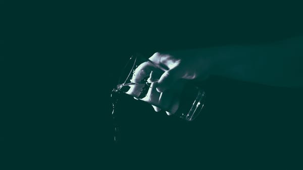 A hand tips out water from a tall glass.