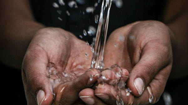 A pair of outstretched hands collect water from a spout.
