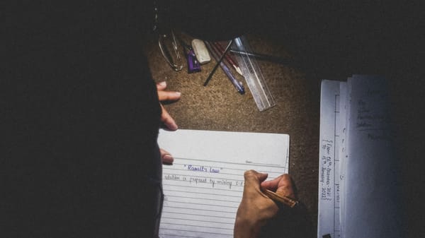 A person writes under the glow of a desk lamp.